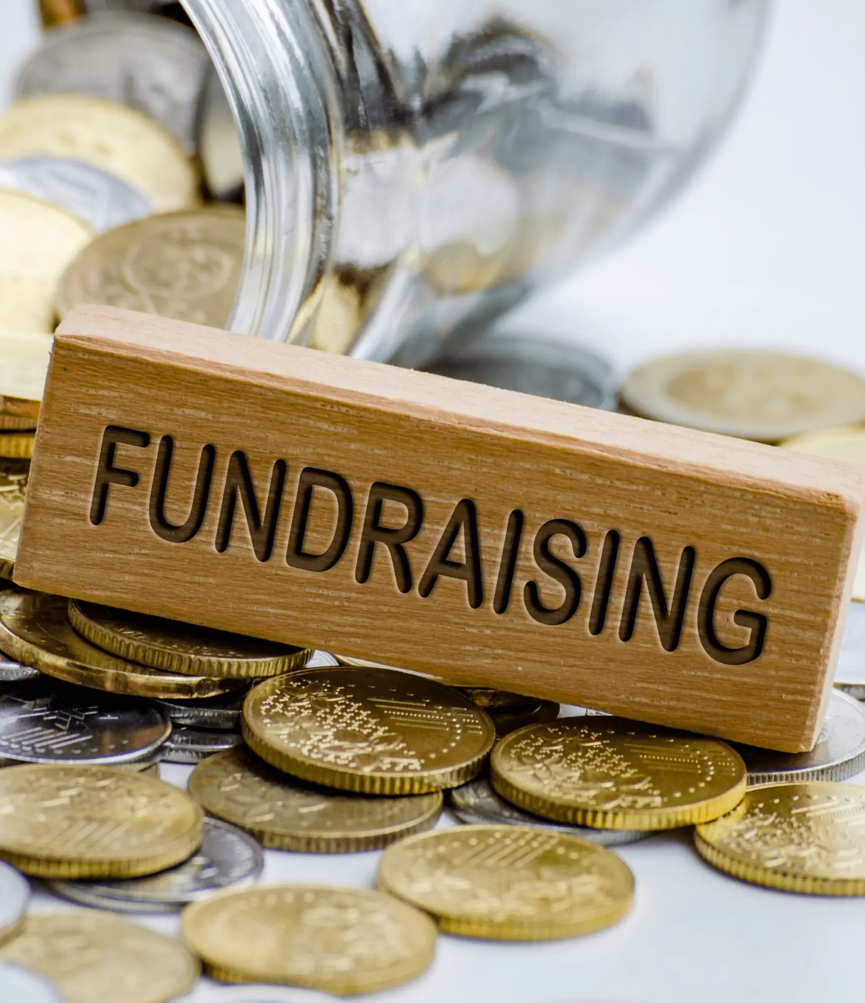 Wooden block labeled 'FUNDRAISING' on coins with a jar in the background.